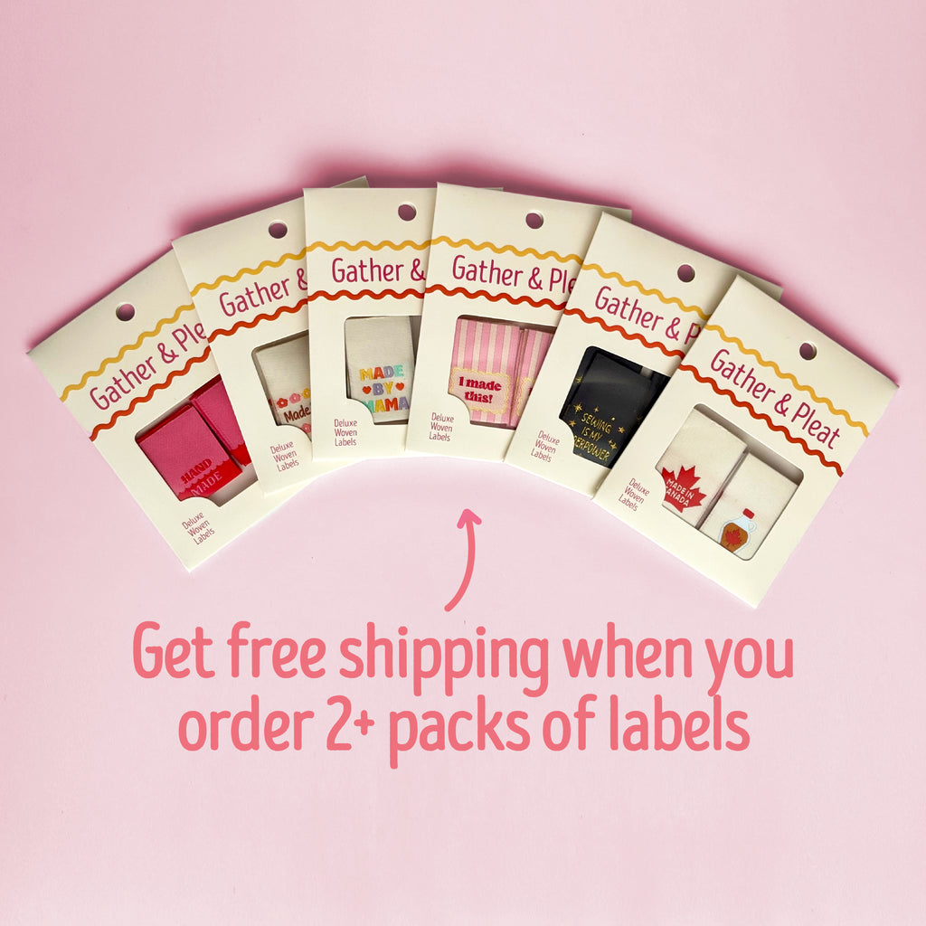 Six woven sewing label packs fanned out on a light pink background, with pink text below reading 'Get free shipping when you order 2+ packs of labels.' The packs feature Gather & Pleat branding and show different label designs and colours inside.