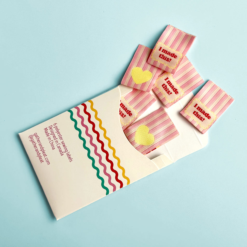 'I Made This!' woven sewing labels displayed beside opened Gather & Pleat packaging showing all six labels included in the pack.