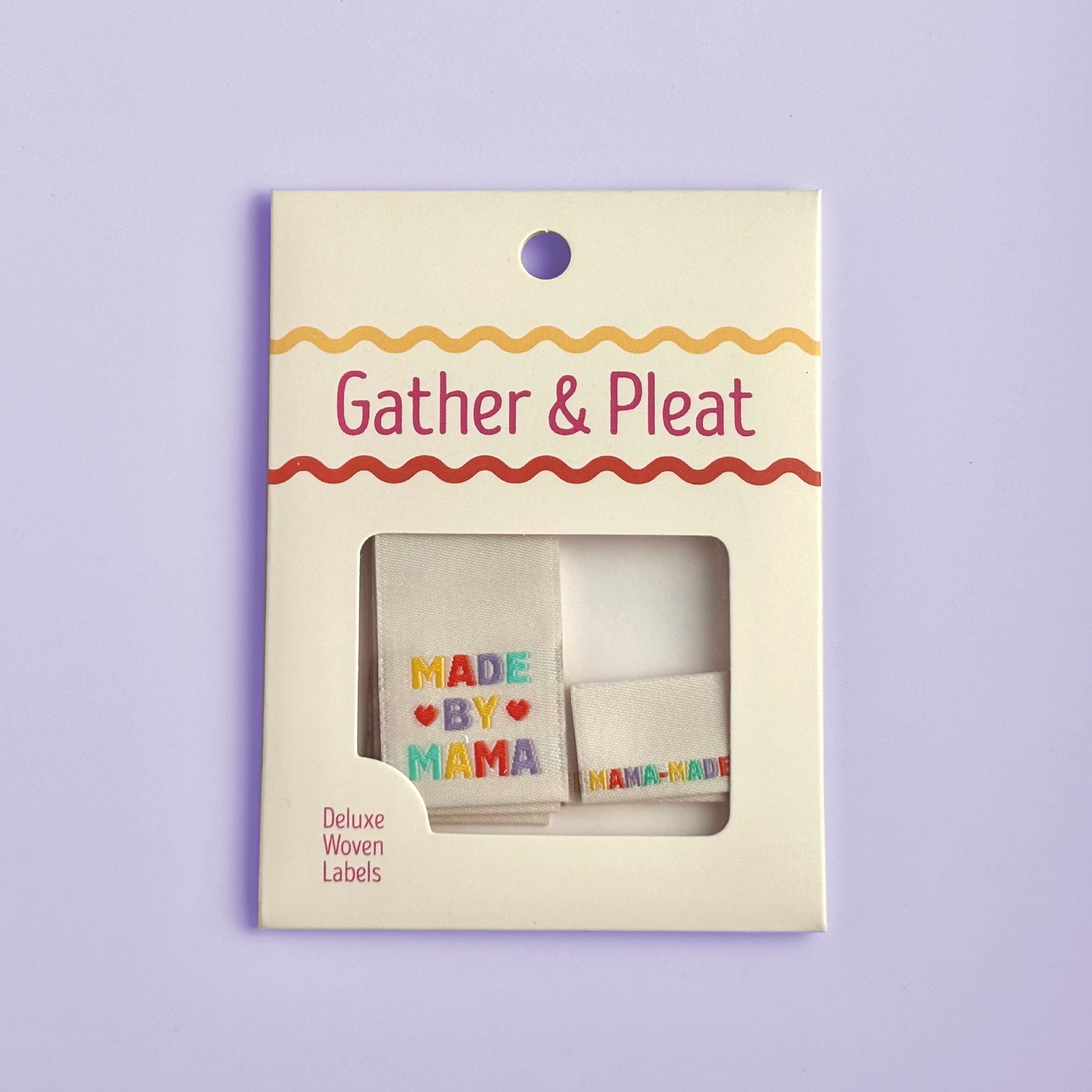 Pack of six 'Made by Mama' woven sewing labels in Gather & Pleat retail packaging, on a lilac background.