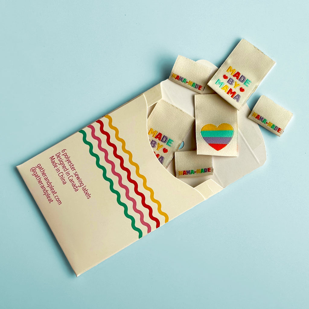 'Made by Mama' woven sewing labels displayed beside opened Gather & Pleat packaging showing all six labels included in the pack.