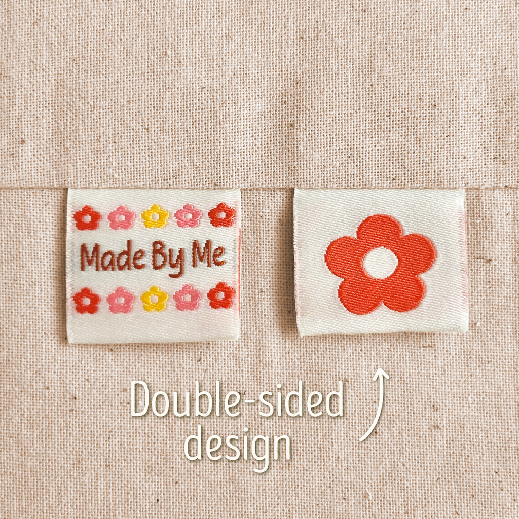 Two small embroidered fabric patches on a beige woven fabric background. The left patch reads “Made By Me” with small multicoloured flowers around it, and the right patch shows a larger red flower. Text in the image explains that this is a double-sided design, implying that the flower is on the back of the 'Made By Me' design.